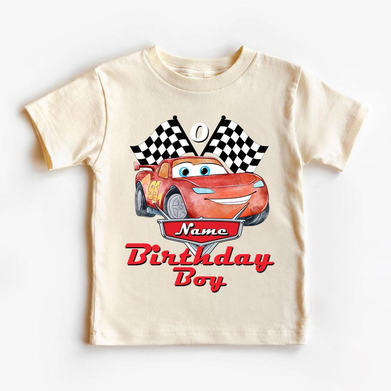 May include: A cream-colored t-shirt featuring a red cartoon race car with the number 95. Above the car are two checkered flags. The shirt has the words "Name Birthday Boy" in red script.