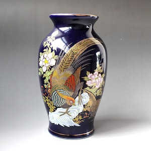 May include: A deep blue ceramic vase featuring a detailed illustration of a pheasant with gold, red, and brown plumage standing on a white rock. The design includes white and pink floral accents with green leaves and a thin gold rim at the top and base.