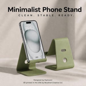 May include: Two sage green phone stands with a smooth finish, one holding a smartphone displaying the time 19:57. The text reads: Minimalist Phone Stand, CLEAN. STABLE. READY. Designed by HpInvent, 3D printed in the USA by Boudinot Creative LLC.