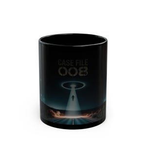 May include: Black ceramic mug with a sci-fi design. The mug features the text "CASE FILE 003" and an illustration of a person being beamed up by a UFO over a road. The background shows a night sky and desert landscape.