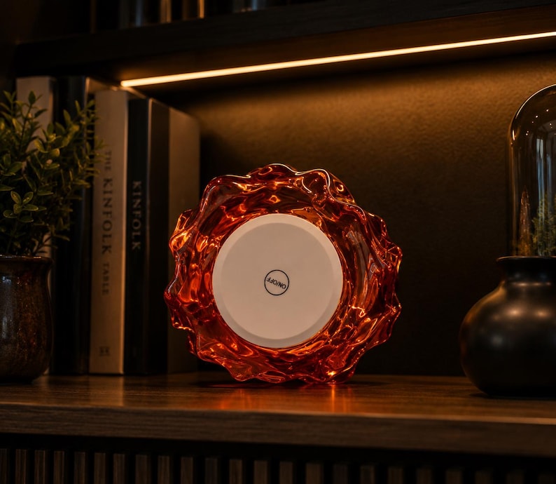 May include: A circular, amber-colored glass light fixture with a wavy, organic edge. The center features a flat, white circular panel with a black button in the middle labeled ON/OFF. The glass has a translucent, rippled texture throughout.