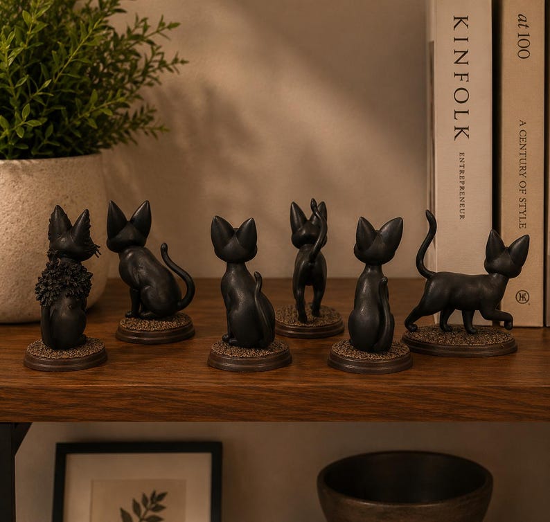 May include: A collection of six small black cat figurines displayed on a wooden shelf. Each cat is depicted in a different pose, including sitting, standing, and walking, and is mounted on a circular base with a textured, brown, ground-like finish.