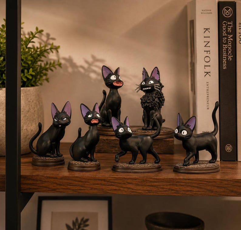 May include: A collection of six black cat figurines with purple-lined ears, each standing on a circular base. The cats are depicted in various poses, including sitting, standing, and one with a textured, curly coat, all featuring large eyes.