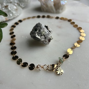 May include: A gold chain anklet with a clover charm and a clear crystal bead. The anklet is made of small, round gold discs.