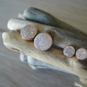 May include: Three pairs of round white sparkly earrings with gold settings. The earrings are arranged in a row on a piece of driftwood.