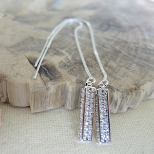 May include: A pair of silver dangle earrings with a rectangular crystal design. The earrings have a long, thin chain that hangs from the crystal.