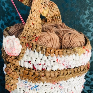 May include: A brown crocheted basket made from recycled plastic bags, with a handle and a brown yarn ball inside.