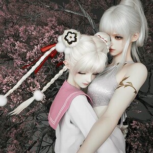 May include: An artistic image featuring two figures with pale skin and white hair, embracing. One figure wears a pink and white uniform, the other a silver top. The background includes pink flowering branches and a dark gray backdrop.