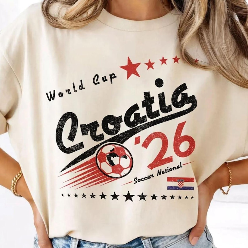May include: A cream-colored t-shirt featuring a graphic with the text World Cup Croatia '26. The design includes a red soccer ball, a series of red stars, a small Croatian flag, and black text with a distressed texture on the front.