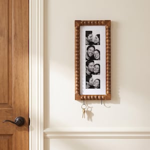 May include: A rectangular wooden wall-mounted photo frame with a beaded border design. The frame holds a vertical strip of four black and white photographs showing a couple. Two metal hooks are attached to the bottom, with a set of keys hanging.