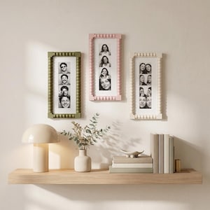 May include: Three rectangular wall frames with beaded edges in olive green, soft pink, and cream. Each frame holds a vertical strip of four black and white portrait photographs. The frames are arranged horizontally on a wall above a wooden shelf.
