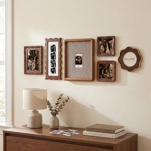 May include: A gallery wall arrangement of six wooden picture frames in various shapes and sizes, including rectangular, square, and scalloped designs. The frames display black and white photographs and one circular frame contains the text US, LATELY.