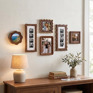 Op de afbeelding: Een verzameling van vijf houten fotolijsten in verschillende vormen en maten aan een muur. De lijsten hebben golvende, kralen- en gladde rechthoekige ontwerpen en tonen diverse foto's van mensen en landschappen in een galerijopstelling.