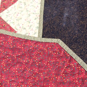 May include: A red quilted fabric with a pattern of small green leaves and yellow dots. The fabric is bordered with a green trim.
