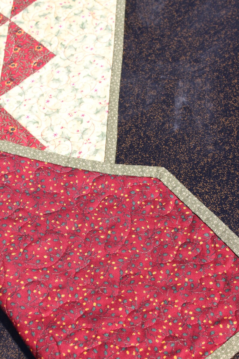 May include: A red quilted fabric with a pattern of small green leaves and yellow dots. The fabric is bordered with a green trim.