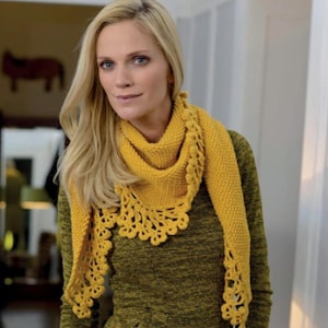 May include: A woman wearing a yellow knitted scarf with a scalloped lace edge. The scarf is draped around the neck and shoulders, and the woman is wearing a green jumper. The scarf is a bright, sunny yellow colour.