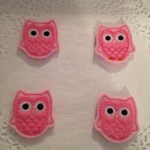 May include: Four pink felt owl appliques with black eyes and white pupils. The owls are on a white doily background.