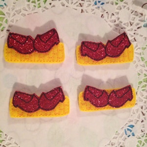 May include: Four pairs of red glitter shoes on a yellow brick road. The shoes are a popular symbol from the Wizard of Oz.