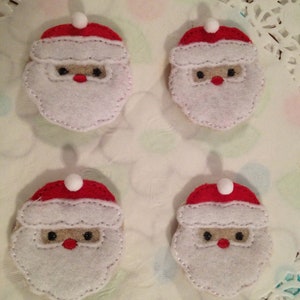 May include: Four felt Christmas ornaments shaped like Santa Claus heads. Each ornament has a white beard, red hat, and black eyes.