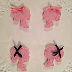 May include: Four pink felt cutouts of a woman's profile with hair. Two have pink bows and two have black bows.