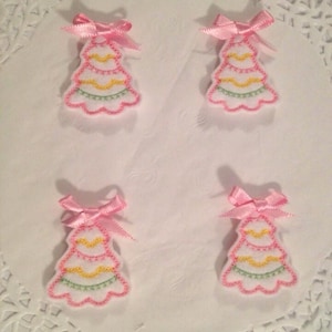 May include: Four pink felt Christmas tree ornaments with green and yellow embroidery. Each ornament has a pink bow.