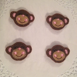 May include: Four brown felt monkey face appliques with pink embroidered cheeks and a stitched smile.