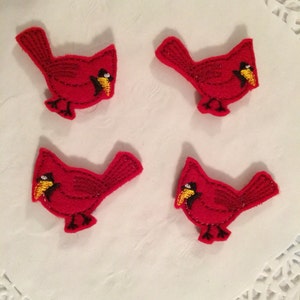 May include: Four red felt cardinal bird appliques with black eyes and yellow beaks. The appliques are on a white background.
