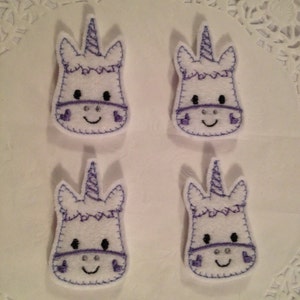 May include: Four white felt unicorn head appliques with purple embroidered details. The unicorns have a purple horn, eyes, and a purple band around their head.