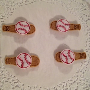 May include: Four felt baseball and bat hair clips. Each clip features a brown felt bat with a white felt baseball with red stitching.