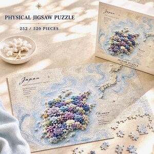 May include: A physical jigsaw puzzle featuring a map of Japan, with a floral design. The puzzle has 252/520 pieces. The box and assembled puzzle are visible, along with some loose pieces. The color palette includes blue, purple, and white.
