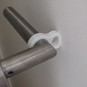 Könnte beinhalten: Nahaufnahme eines Türgriffs aus Edelstahl mit einem Türgriffstopper aus weißem Kunststoff. Der Griff ist an einer weißen Wand befestigt. Der Stopper ist ein kleines, gebogenes Teil.