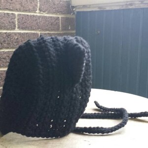 May include: A black knitted hat with a long, thick cord. The hat is made of a soft, textured yarn.