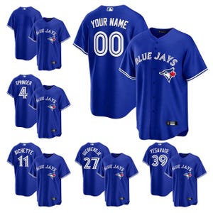 Puede incluir: Una colección de camisetas y camisetas de béisbol azules. Las camisetas muestran el texto "BLUE JAYS" y los nombres y números de los jugadores. Las camisetas tienen el logotipo de "BLUE JAYS". Las camisetas tienen ribetes blancos.