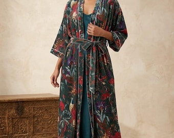 May include: A long, dark green velvet robe with a floral pattern in red, purple, and yellow. The robe has a matching belt and white trim along the edges. The model is wearing a teal dress underneath. The robe is approximately 55 inches long.