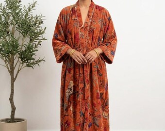 May include: An orange floral patterned robe with white trim. The robe has a belt and long sleeves. The fabric appears to be velvet. The robe is knee-length and has a V-neck. The model is wearing gold jewelry.
