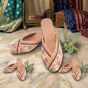 May include: A pair of blush-colored embroidered slippers with floral and geometric patterns. The slippers have a pointed toe and a flat sole. The embroidery includes pink, green, and yellow flowers with black and gold accents. Additional pairs are also shown.