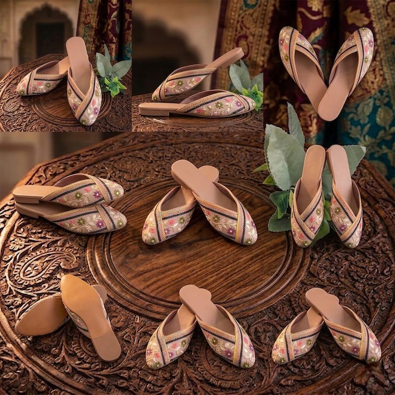 May include: An assortment of embroidered slip-on shoes with a floral design. The shoes feature a beige base with colorful floral embroidery, black trim, and a light brown sole. The shoes are displayed on a carved wooden surface.