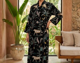 May include: A black robe with a jungle print featuring leopards, birds, and palm trees. The robe has a wrap-around design with a matching belt. The long-sleeved robe is worn by a person standing in front of a large window.