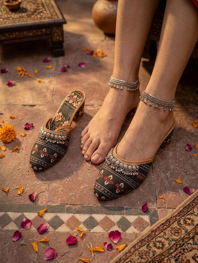 Puede incluir: Un par de zapatos sin cordones con estampado negro y rojo con adornos plateados. Los zapatos se muestran con un par de tobilleras plateadas a juego. Los zapatos tienen un tac&oacute;n peque&ntilde;o y est&aacute;n decorados con motivos florales.