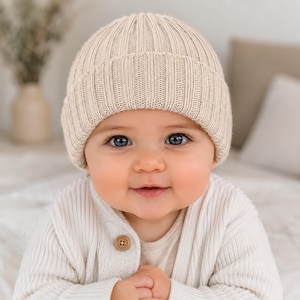 May include: A beige ribbed knit beanie hat with a folded cuff, worn on a head. The hat features a vertical textured pattern throughout the fabric, providing a consistent knit appearance across the entire surface of the headwear accessory.