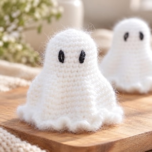 Può includere: Due piccole figure di fantasmi lavorate all'uncinetto in bianco con texture di filato soffice. Ogni fantasma presenta due semplici occhi ricamati in nero orientati verticalmente. Le figure hanno una parte superiore arrotondata.
