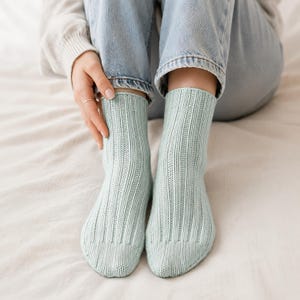 Peut inclure: Une paire de chaussettes mi-mollet vert menthe clair avec un motif en tricot côtelé vertical. Les chaussettes présentent un design simple et épuré avec un bout arrondi et un bord droit, offrant une texture uniforme sur tout le vêtement.