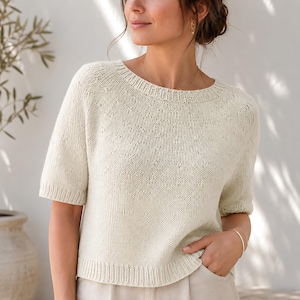 Può includere: Un maglione in maglia color crema a maniche corte con scollo rotondo e un sottile motivo testurizzato sul carré. Il capo presenta dettagli a coste sul colletto, sui polsini delle maniche e sull'orlo, offrendo una finitura strutturata.