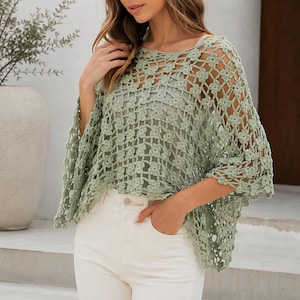 Könnte beinhalten: Hellgrünes Häkeltop mit floralem Muster. Das Oberteil hat ein lockeres, offenes Design mit weiten Ärmeln. Das Model trägt das Oberteil mit einer weißen Hose.