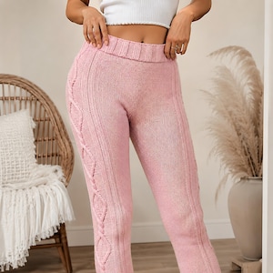 Peut inclure: Legging en tricot rose clair doté d'une large ceinture côtelée et de détails en torsades verticales le long des côtés extérieurs de chaque jambe. Le vêtement est fabriqué dans une matière en fil texturé d'une couleur rose douce et uniforme.