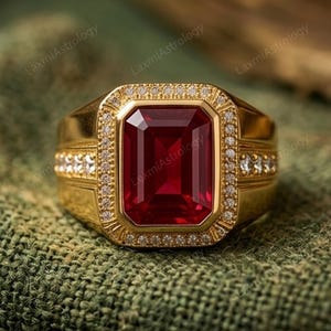 Könnte beinhalten: Ein goldener Ring mit einem großen, rechteckigen, tiefroten Edelstein in der Mitte. Der Edelstein ist von einem Kranz aus kleinen, klaren Steinen umgeben. Zusätzliche kleine Steine sind am Ringband angebracht.