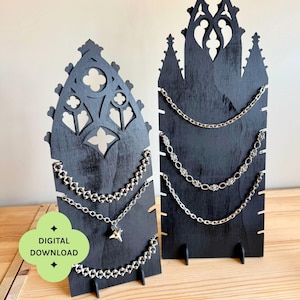 May include: Two black wooden jewelry display stands with pointed gothic-style arches and cut-out details. The stands feature side notches for holding silver-toned metal chains. A green graphic overlay includes the text DIGITAL DOWNLOAD and LASER CUTTING FILE, 2 DISPLAYS.