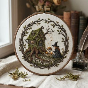 May include: Embroidered artwork in a wooden hoop. The design features a whimsical green cottage nestled in a tree trunk, surrounded by a leafy frame. A figure in a black dress and witch hat kneels near mushrooms.