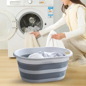 May include: An oval-shaped, collapsible laundry basket featuring a white rim and base with alternating gray and white flexible silicone side panels. The basket is designed with integrated handles on both sides for easy carrying and storage.