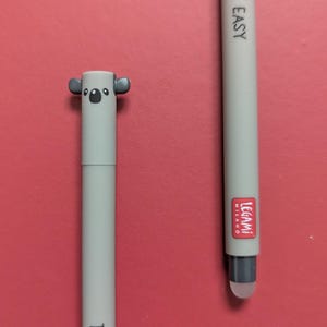 May include: Two light grey pens with a koala-themed cap on one and a stylus tip on the other. Both pens feature the text "TAKE IT EASY" printed in black. One pen displays a red "LEGAMI MILANO" logo near the bottom. The pens have a smooth finish.